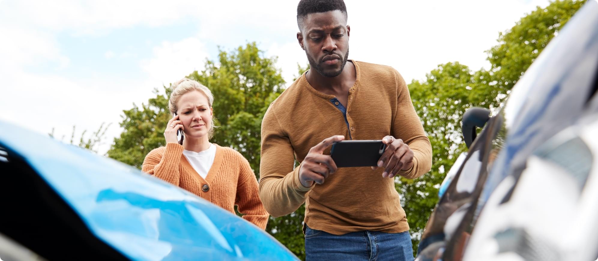 Woman calls in an accident while young man takes pictures of damage for car insurance claim.
