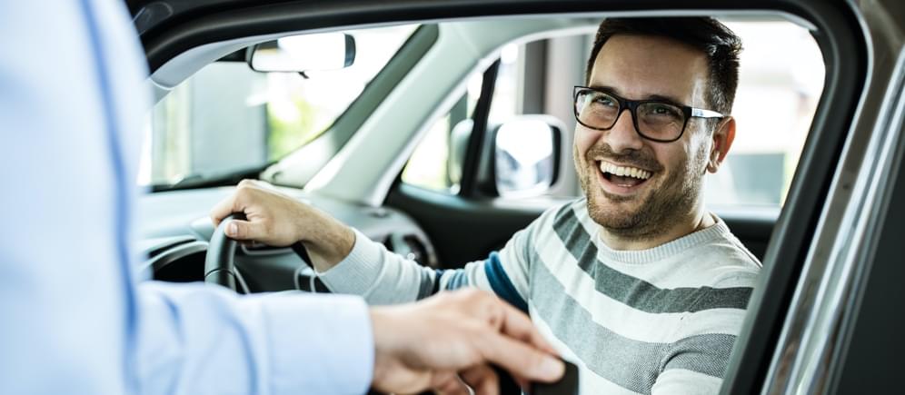 Smiling man is buying a new car which is why is he is looking for cheap auto insurance online.